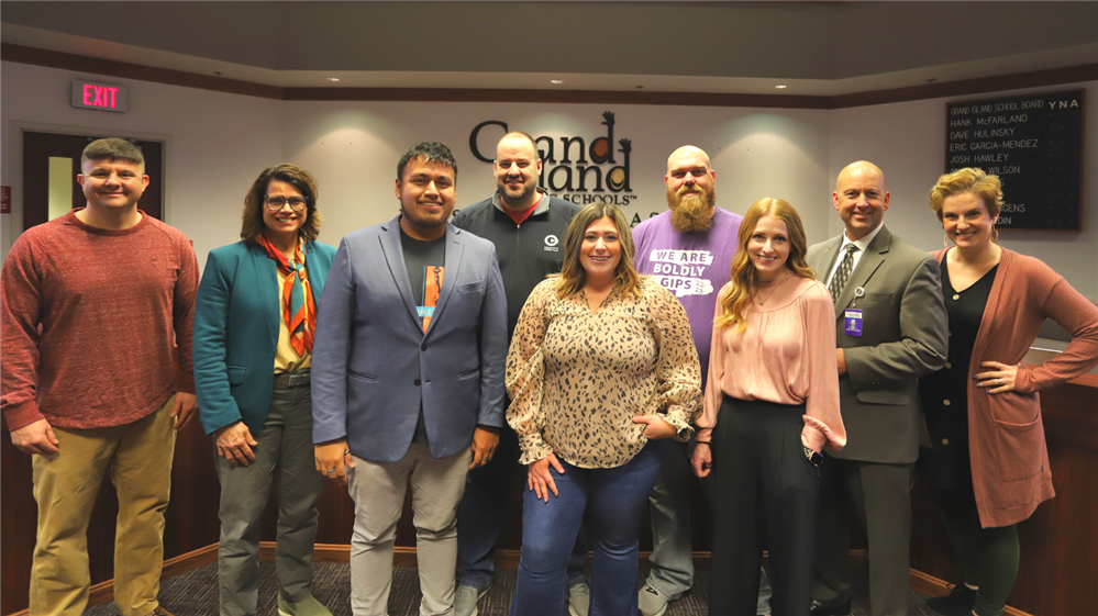 GIPS Board of Education members standing in the board room and smiling in front of the GIPS logo.